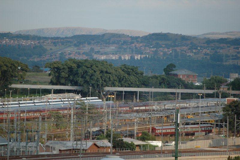 The City of Pretoria with, its railway infrastructure, makes an interesting vista. The foreground behind the brick building one can see the Friends of the Rail steam hauled train heading out towards the main line to Germiston. The Gautrain development can be clearly seen and the associated railway dÃ©cor. Viewed with a telephoto lens from the UNISA campus building.