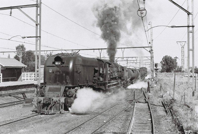 Double GMAM Garratts haul a ballast train out the "hole" alongside the Koedoespoort railway workshops, from the ballast sidings. The train would then draw in to the Koedoespoort station, the locos  run around the load and proceed out to Pretoria station and then the main line to Johannesburg, before taking the turn at Olifantsfontein station and heading off to the new yard at Sentrarand.<br />1980's. All the photos sent are mine.