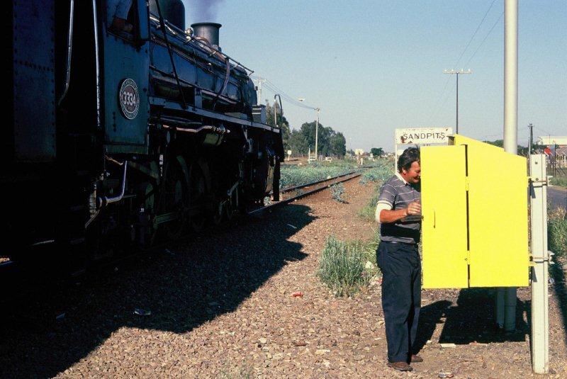 The wooden train staff for the next section, Sandpits to Swartspruit, must first be obtained before the train may proceed. Driver Cliff Petzer is removing it from its housing, while the 19D 3344 stands ready to head out to Magaliesburg. The line is today in pieces, one here and the others overseas! The locomotive is at George in the Cape after a transfer in the mid 1990s. The wooden train staff working still occurs on the branch from Rayton to Cullinan.