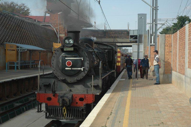 Class 24 number 3664 JoAnna has a short stop at Rissik station. The Gautrain Hatfield terminal is at this point and their formation can be seen on the top right. Michiel Boshoff, with black cap, the TFR college lecturer, stands admiring the steamy side of things.