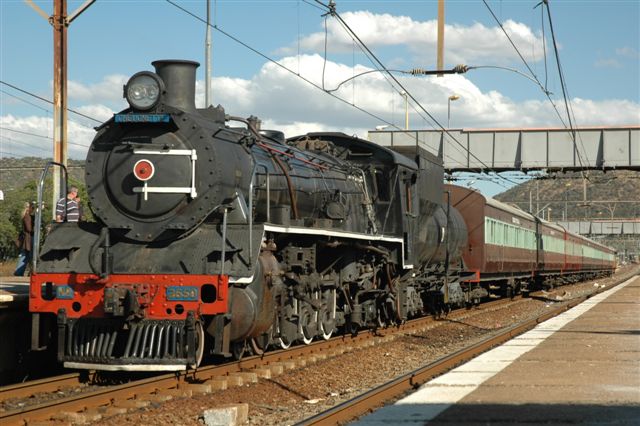 19D 2650 stands at the head of her Pienaarsrivier locol train. This service was in its last days, prior to dieselisation and final withdrawal of the service. Seen here picking up passengers at Pretoria North.<br /><br />That's how it used to look in the early 1970's, and so nice that FOTR have retained the colour scheme and type of coaching set, so typical of the steam suburban period throughout the country.